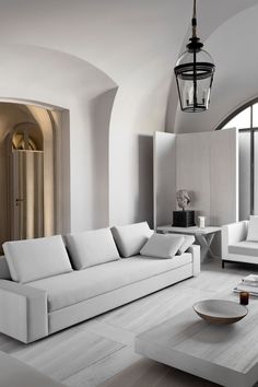 a living room filled with white furniture next to a large window and a chandelier