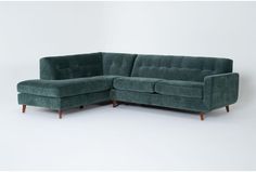 a green sectional couch sitting on top of a white floor next to a wooden frame