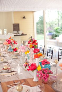 the table is set with colorful flowers in vases and place settings for guests to sit at