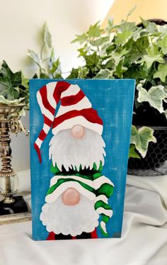 a painting of santa claus on a blue background next to potted plants and greenery