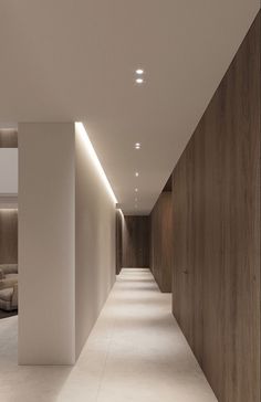 a long hallway with white walls and wood paneling on the sides is lit by recessed lights