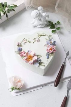 a heart shaped cake sitting on top of a cutting board next to flowers and a knife