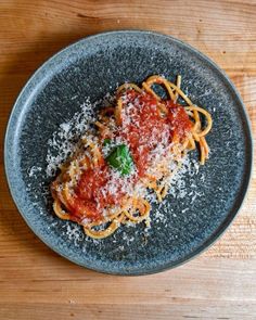 a plate of spaghetti with sauce and parmesan cheese on top, sitting on a wooden table