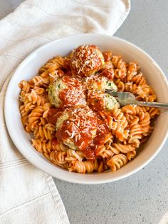 a white bowl filled with pasta and meatballs covered in marinara sauce on top of a white towel