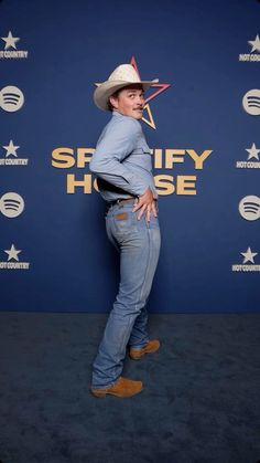 a man wearing a cowboy hat and jeans standing in front of a blue wall with the words sheriff house on it