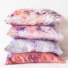 three pillows stacked on top of each other in front of a white wall with paint splatters all over them