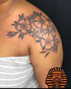 a woman's shoulder with flowers on it and an egyptian symbol in the middle