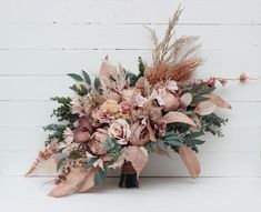 a bridal bouquet with dried flowers and greenery on a white wooden table top