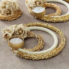 three gold and white wreaths with flowers on them sitting on the floor next to candles