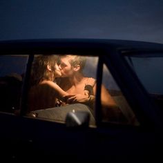 a man and woman sitting in the back seat of a car at night, kissing