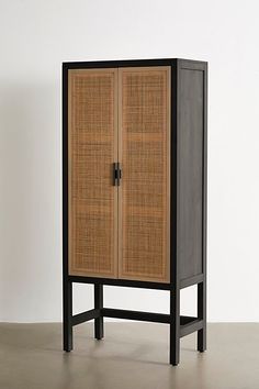 the cabinet is made out of wood and has black metal legs, with a rattan door