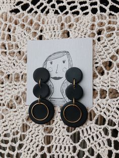 the black and gold earrings are on top of a white doily with an image of a woman's face