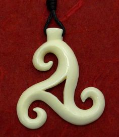 a white ceramic pendant on a black cord hanging from a red velvet surface, with the letter s in the center