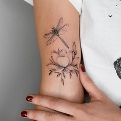 a woman's arm with a dragonfly on it and flowers in the foreground