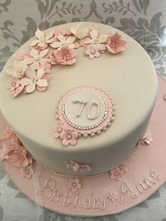 a white cake with pink flowers and the number seventy on it is sitting on a table