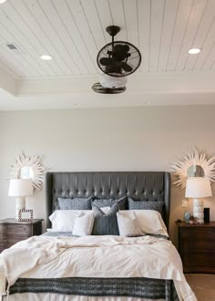 a large bed sitting under a ceiling fan next to two nightstands in a bedroom