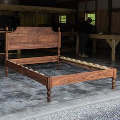 a wooden bed frame sitting on top of a cement floor next to a window and table