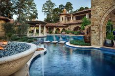 an outdoor swimming pool surrounded by stone pillars and arches, with a fountain in the middle