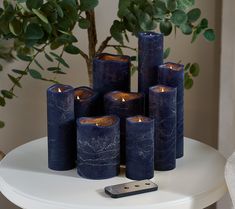 several blue candles sitting on top of a white table next to a cell phone and potted plant