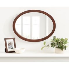 a round mirror sitting on top of a white shelf next to a potted plant