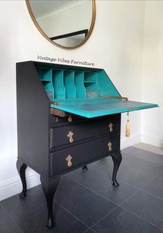 an antique desk with blue drawers and gold handles is shown in front of a round mirror