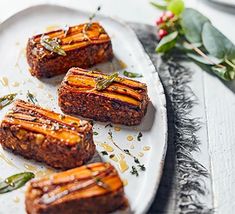 four pieces of meat on a white plate with herbs and flowers in the back ground