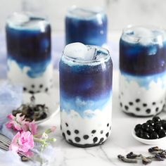 blue and white drinks with blackberries in them on a marble counter top next to flowers