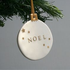 a ceramic ornament with the word noel hanging from a christmas tree branch in front of a gray background