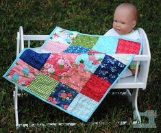 a baby doll sitting on top of a white bench next to a patchwork quilt