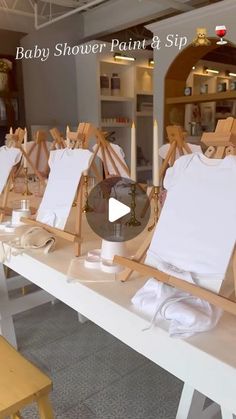 the baby shower paint and sip table is set up with clothes on easels for display