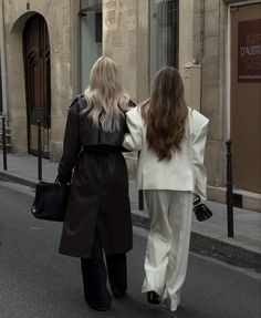 two women walking down the street with their back to each other, both carrying bags