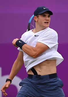 a man holding a tennis racquet on top of a tennis court with a purple wall in the background