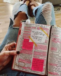 a person sitting on the floor holding an open book with sticky notes attached to it