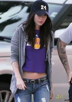 a woman in ripped jeans and a baseball cap is walking with her hand on her hip