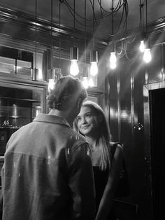 black and white photograph of man and woman in kitchen looking at each other with light bulbs overhead