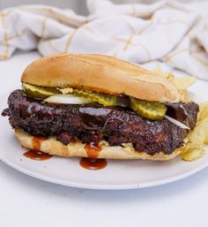 a steak sandwich with pickles and onions on a plate next to some potato chips