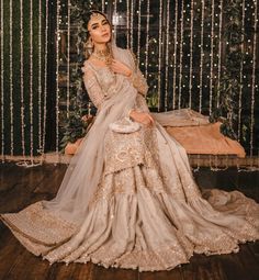 a woman in a wedding dress sitting on a wooden floor next to a wall with lights