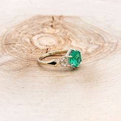 an emerald and diamond ring sitting on top of a piece of wood