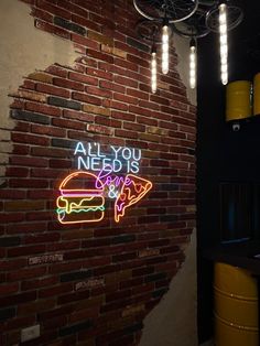 all you need is burger and fries neon sign on brick wall with lights hanging from the ceiling