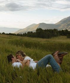 a man and woman laying in the grass with mountains in the background