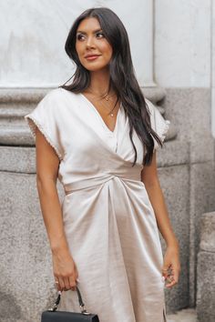 Elevate your wardrobe with this versatile and luxurious dress. Perfect for any occasion! This Champagne Satin Wrap Midi Dress boasts a sophisticated v neckline and elegant fringe detail. Made from 100% polyester, it offers both style and comfort in one stunning piece. Pair it with strappy high heels, elevated gold jewelry, and a neutral crossbody bag for a chic evening outfit! Elegant Short Sleeve V-neck Dress For Date Night, Elegant Short Sleeve V-neck Dress For Brunch, Glamorous V-neck Fringe Dresses, Fringe V-neck Dress For Night Out, Chic Silk V-neck Mini Dress, Elegant Mini Dress With Notched Neckline For Summer, Evening V-neck Mini Dress With Fringe, Elegant V-neck Dress With Notched Neckline For Date Night, Elegant Satin Midi Dress With Surplice Neckline