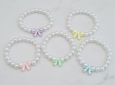 Cute pastel coloured bow and pearl bracelet.  Choose your colour to suit your bridal party.  The bracelet is made from 8mm glass pearls in either white or off white.  Choose from pale pink, lilac, yellow, green or blue acrylic bow.  For example when ordering:  Blue bow and off white pearls or green bow and white pearls. This bracelet is stretchy and has no clasp so it can be slipped over the hand. If you would like to personalise the bracelet with an engraved initial, then please use this link: https://www.etsy.com/uk/listing/401138481/extra-initial-tag-additional-initial-tag?click_key=9f7afd697f108120d760450d7f05a8c9644b4865%3A401138481&click_sum=11ac29c5&ref=shop_home_active_1&sts=1 Please see approximate size guide below: Sizes for children 12-24 months    5in 2-3 years    5.0-5.5in 4-5 Elegant Pastel Bracelets For Gifts, Elegant Pastel Bracelets As Gift, Cute White Bracelets For Party, Cute White Party Bracelets, Bridal Party Bracelets, Party Bracelets, Bracelets Cute, Flower Girl Jewelry, Bracelet Flower