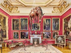 a room filled with paintings and a large horse statue hanging from the ceiling over a fire place