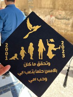 a person holding up a black and gold graduation cap with images of people on it