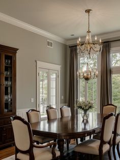 a dining room table and chairs with chandelier hanging from the ceiling in front of windows