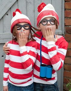 two children wearing red and white striped sweaters, one holding his face to the other's mouth