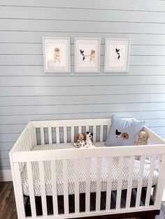 a white crib with two pictures on the wall above it and a dog bed