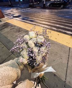 a bouquet of white roses sitting on the side of a road next to a street