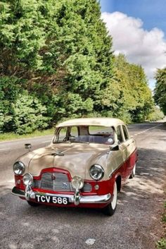 an old car is parked on the side of the road in front of some trees