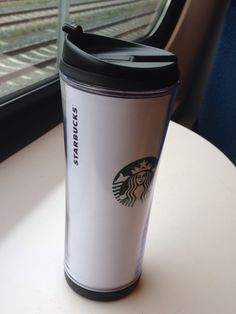 a starbucks cup sitting on top of a white table next to a train window with the word starbucks written on it